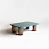 A stylish coffee table with a high gloss blue Birdseye maple wood curved top that sits on upon four round antiqued brushed brass legs. Side view. Design by DAVIDSON London.